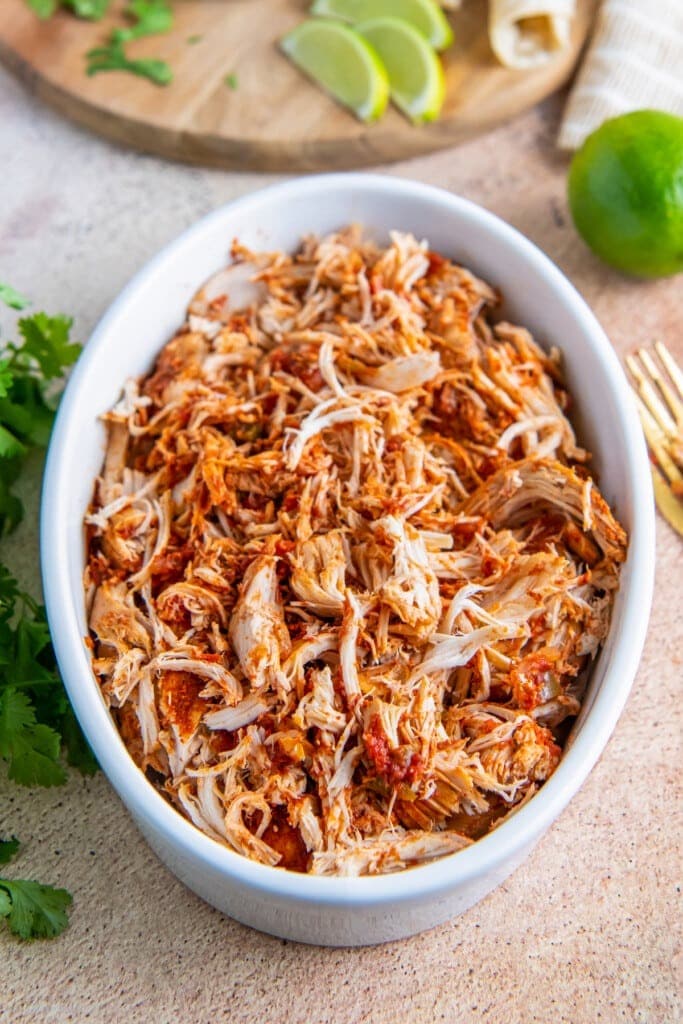 Easy Crockpot Salsa Chicken on a casserole with slices of lime on a wooden cutting board