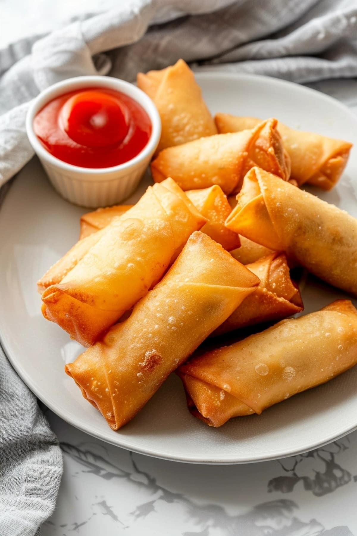 Egg rolls with ketchup dip in a ramekin bowl served on a white plate.