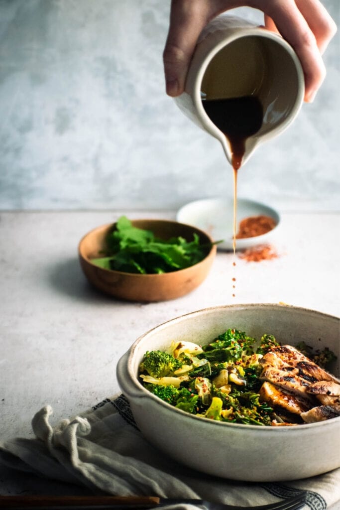 Pouring Soy Sauce into a Bowl of Green Vegetables and Grilled Chicken